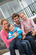 © goodluz - Happy family of 4 people sitting in front of new home