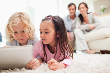 Cute siblings using a tablet computer while their parents are in