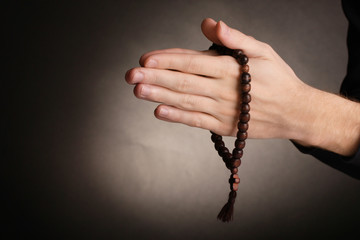 Hands holding wooden rosary on grey background