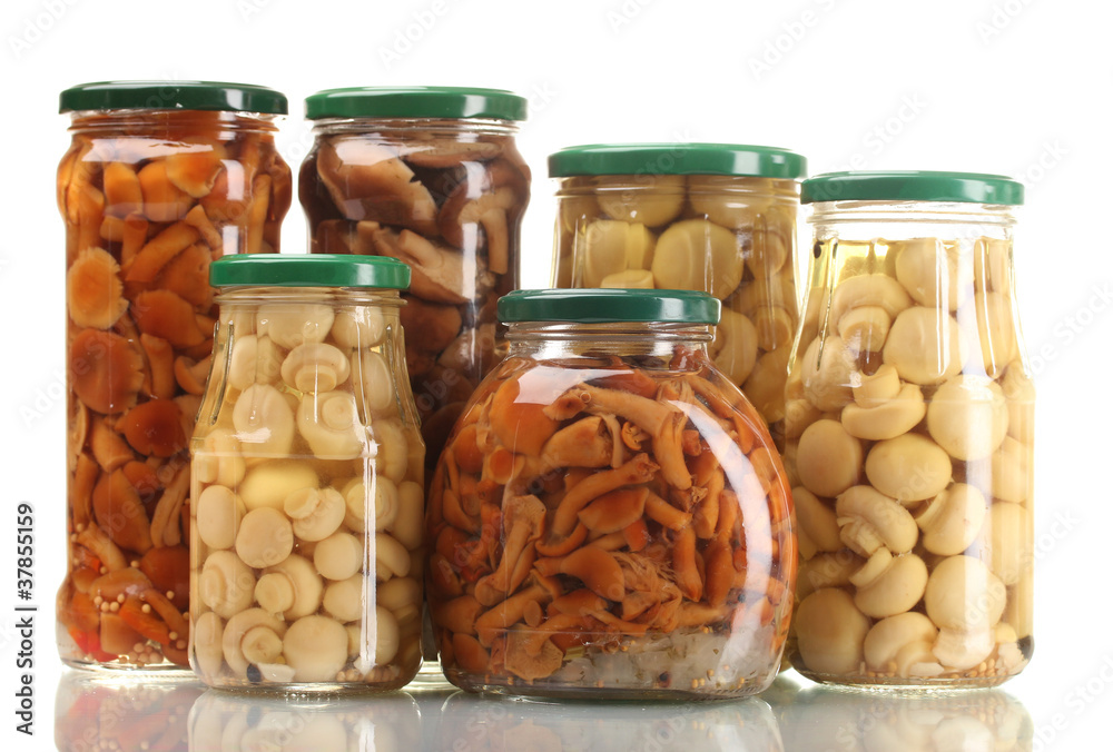 Different glass jars of marinated mushrooms isolated on white