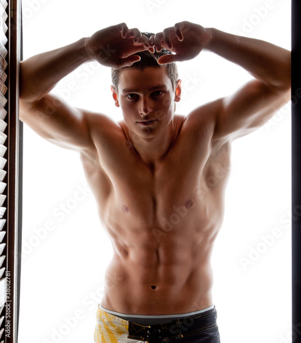 Fototapeta The muscular young naked sexy man leaned against the wall