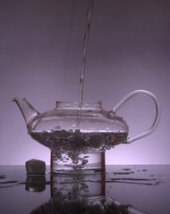 Poster - Water flows into the glass teapot on violet