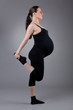 © EwaStudio - Pregnant woman doing gymnastic exercises on grey background.