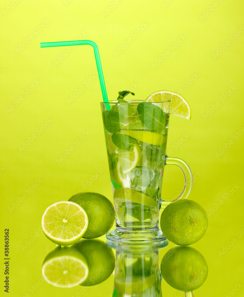 Glass of cocktail with lime and mint on green background
