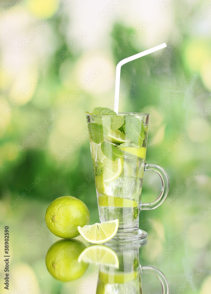 Glass of cocktail with lime and mint on green background