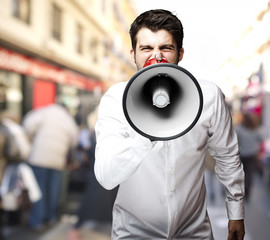 Wall Mural - portrait of young man screaming with megaphone at city