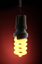 A Lit Energy Saving Light Bulb On Red Background