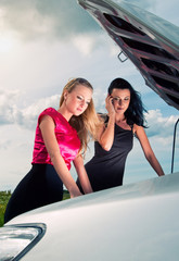 Two young women with broken car on a road