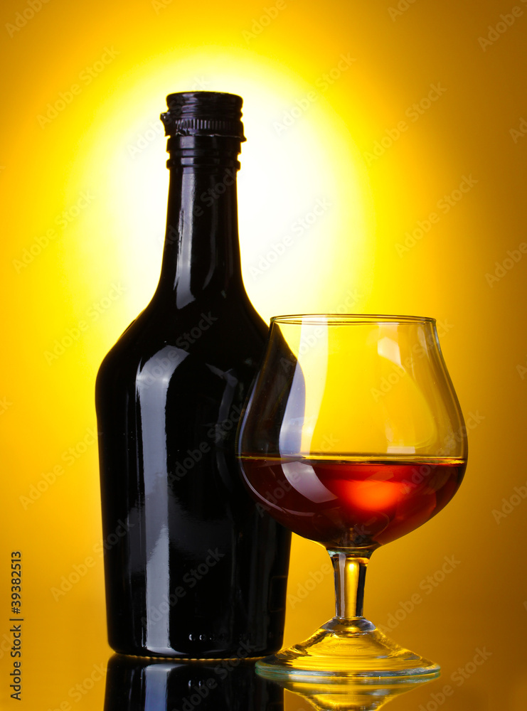Glass of brandy and bottle on yellow background