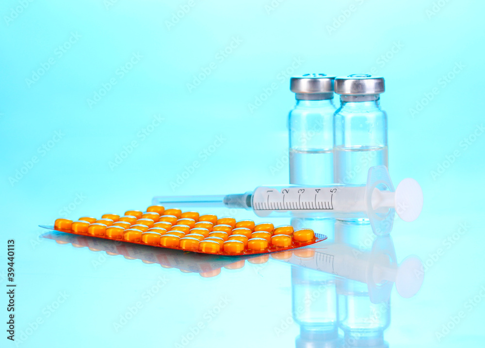 Syringe with medical ampoules and tablets on blue background