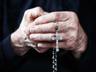 Caucasian elderly hands clutch a Christian rosary in prayer