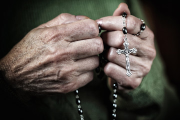  elderly woman's hands tighten a classic Christian rosary for prayer. concept of religious belief and faith, hope.