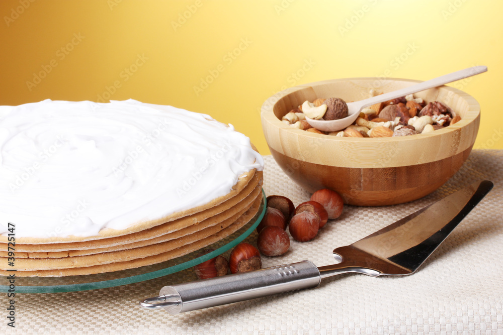 cake on glass stand and nuts on table on yellow background