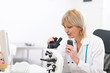 © Alliance - Senior doctor woman looking in microscope and making voice notes