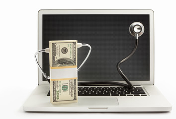 Stack of dollar bills with stethoscope on laptop