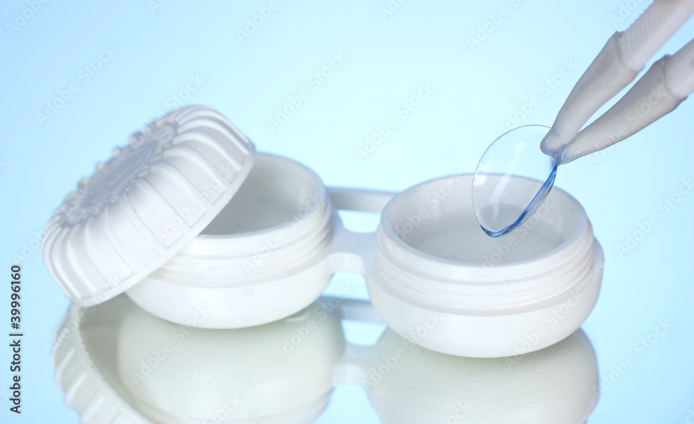 contact lenses in containers and tweezers on blue background