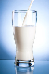 Wall Mural - Pouring a Fresh Glass of Milk on a blue background