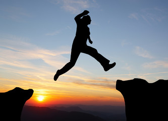 Silhouette of hiking man jumping over the mountains at sunset