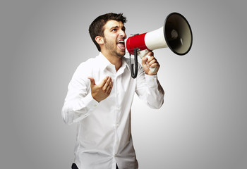 portrait of young man shouting with megaphone over grey backgrou