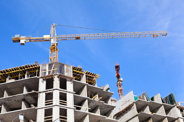 Buildings under construction with cranes on blue sky