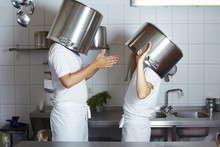 Two Chefs Having Discussion With Large Pans On Their Heads