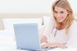 © WavebreakmediaMicro - Woman lying on the bed, with laptop, looking forward and smiling