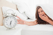 © WavebreakmediaMicro - The woman yawns while trying to silence her alarm clock