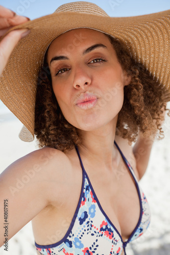 Fotografie, Obraz Young woman puckering her lips while holding her hat brim