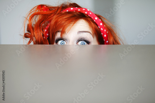 Leinwand Poster  Funny girl hiding behind a table