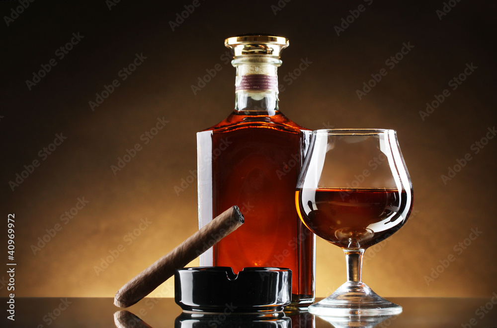 bottle and glass of brandy and cigar on brown background