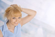 © iulias - Woman leaning against blue background with hand in hair
