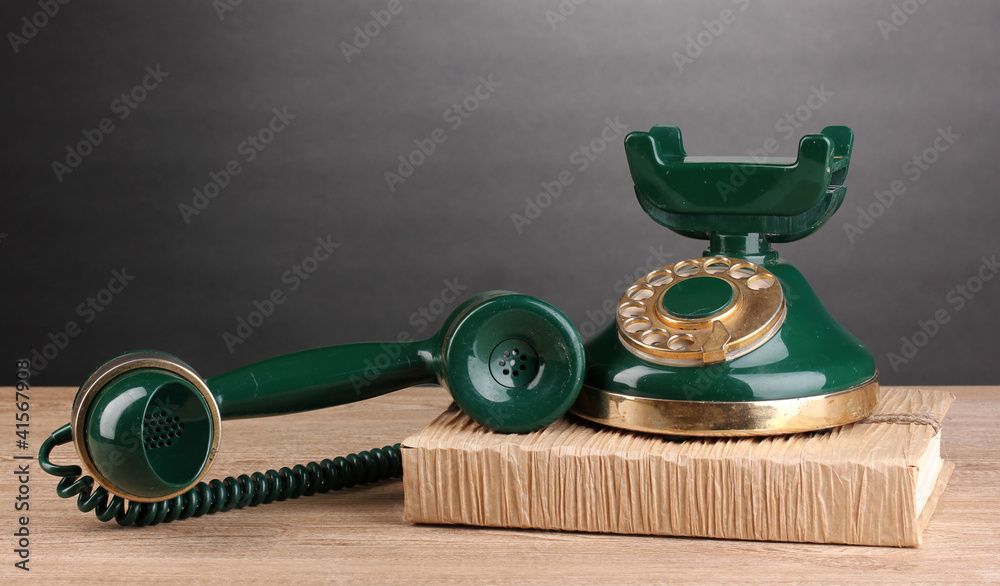 Retro phone standing on book on wooden table on grey background