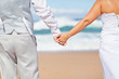 rear view of groom and bride holding hands on beach