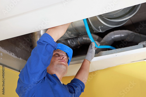 Fotografía Worker holding blue pipe in place under air ducts