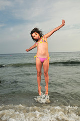 Young happy girl jumping out of the water of sea