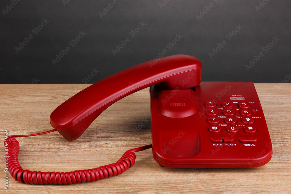 Red phone on wooden table on grey background
