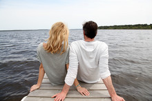 Rear View Of Couple Sitting On A Wooden Bridge By A Lake