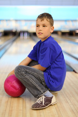 Wall Mural - Boy dressed in T-shirt with ball sits on floor in bowling club