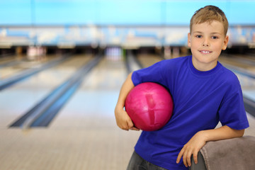 Wall Mural - Happy boy dressed in T-shirt holds pink ball in bowling club