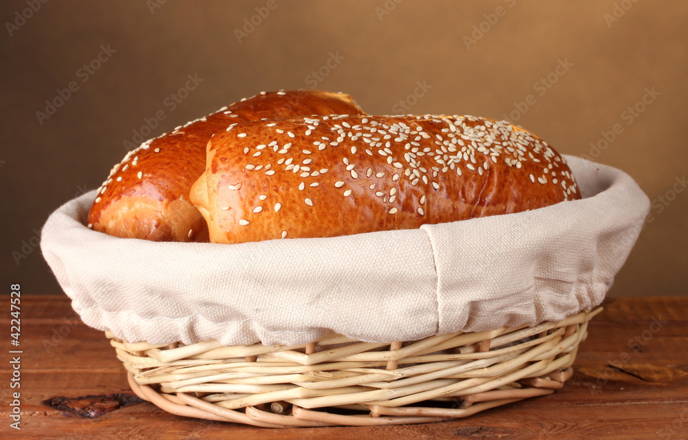 Baked bread in basket on wooden table on brown background