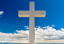 White Cross Against Blue Sky And Fluffy Clouds