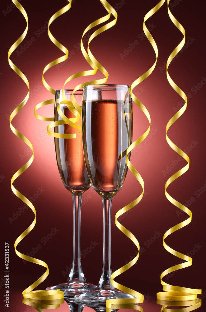 glasses of champagne and streamer on red background
