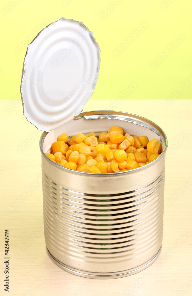 Open tin can of corn on wooden table on green background