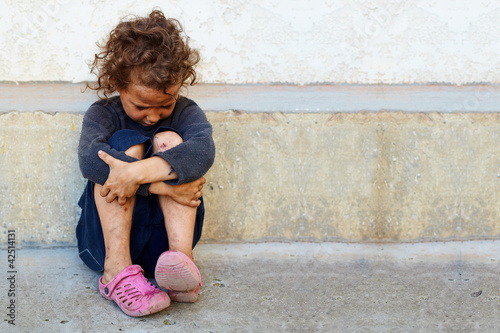 Fotografía poor, sad little child girl sitting against the concrete wall