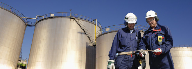 Wall Mural - oil workers with storage towers in background