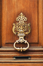 Elegant Carved Door Knocker (handle) Made Of Old Fashioned Vintage Brass Gold Colored Metal With Ancient Brown Door Background As A Symbol Of Resident. Concept Of Luxury Exterior And Rich Life.