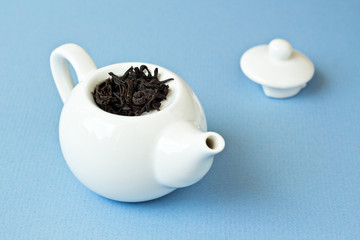 Small tea pot with leaves of black tea on light blue background