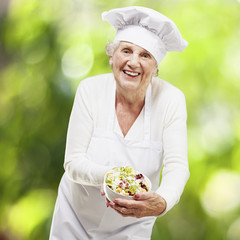 senior woman cook holding a bowl with salad against a nature bac