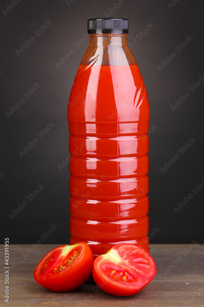 Tomato juice in bottle on wooden table on grey background