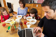 © Monkey Business - Family Using Gadgets Whilst Eating Breakfast Together In Kitchen